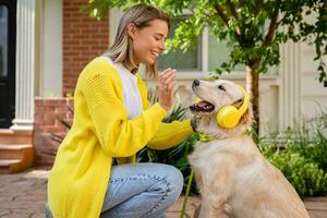 mulher dentro amarelo suéter caminhando às dela casa com uma cachorro ouvindo para música dentro fones de ouvido foto