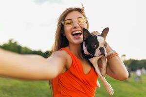 jovem feliz sorridente mulher dentro laranja vestir tendo Diversão jogando com cachorro dentro parque foto