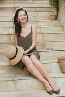 jovem à moda atraente mulher dentro elegante vestir sentado em escadaria, Palha chapéu e saco foto