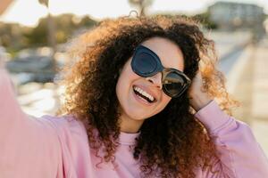 jovem bonita encaracolado mulher dentro oculos de sol em verão período de férias com telefone foto