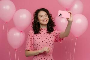 bonita jovem mulher posando isolado em Rosa estúdio fundo com Rosa ar balões e Smartphone foto