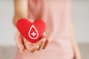 mulher com as mãos segurando um coração vermelho com sinal de doador de sangue. conceito de saúde, medicina e doação de sangue foto