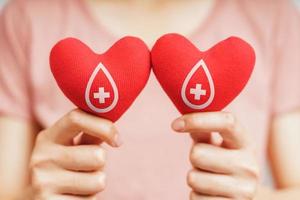 mulher com as mãos segurando um coração vermelho com sinal de doador de sangue. conceito de saúde, medicina e doação de sangue foto