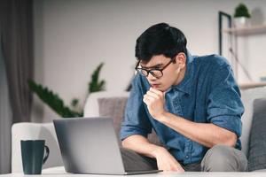 homem asiático sério pensativo pensativo em óculos, olhando para o pensamento de tela do laptop para solução para resolver o problema. foto