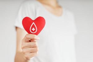 mulher com as mãos segurando um coração vermelho com sinal de doador de sangue. conceito de saúde, medicina e doação de sangue foto