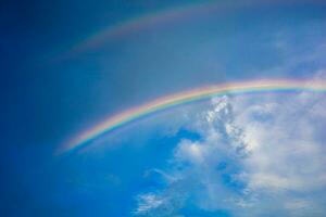 lindo multicolorido arco Iris depois de chuva em a azul céu e branco nuvens. foto