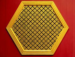 ouro hexágono estêncil janela em a madeira vermelho parede chinês estilo foto