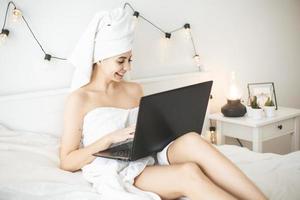 jovem trabalhando na cama branca, usando o laptop. foto