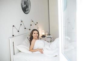 bela jovem acordando em uma cama confortável com lençóis brancos e frescos. foto