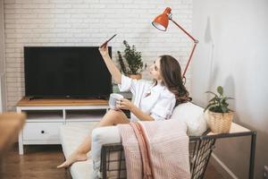 jovem faz selfie sentado no sofá em casa. foto