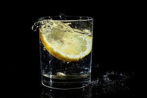 água com limão em um copo em um fundo preto. foto