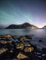 aurora boreal com estrelas sobre a montanha com pedras na costa foto