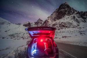 homem turista sentado no carro traseiro em uma montanha cercada pela aurora boreal foto