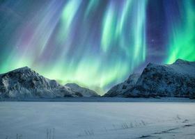 aurora boreal, aurora boreal acima na montanha nevada na praia skagsanden nas ilhas lofoten foto