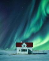 aurora boreal sobre casa branca na neve no inverno