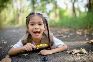 uma pequeno ásia menina usando uma lupa para estude uma veado besouro dentro uma parque. foto