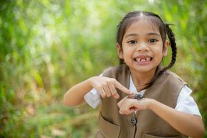 uma pequeno ásia menina usando uma lupa para estude uma veado besouro dentro uma parque. foto