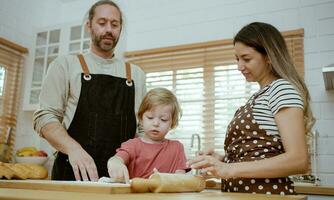 pai e mãe ensino bebê filho amassar massa em cozinha contador às lar. pais e Garoto criança apreciar e Diversão dentro de casa atividade cozinhando junto. foto