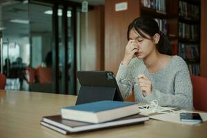 ásia aluna mulher ler livros dentro biblioteca às universidade. jovem menina estresse cansado ter problema enquanto estude duro. tristeza conceito foto