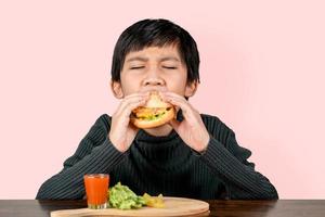 menino asiático fofo comendo um hambúrguer delicioso de felicidade foto