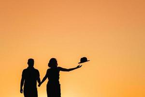 silhuetas de um jovem casal feliz em um fundo de pôr do sol laranja no deserto de areia foto