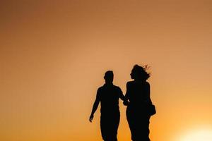 silhuetas de um jovem casal feliz em um fundo de pôr do sol laranja no deserto de areia foto