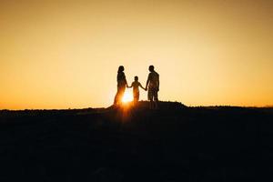 silhuetas de uma jovem família feliz contra um pôr do sol laranja foto