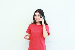 retrato do lindo ásia mulher vestindo vermelho equipamento a comemorar Indonésia independência dia enquanto chamando com sorridente expressão foto