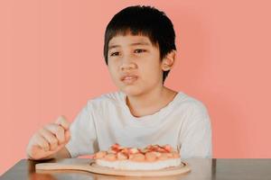 menino bonito asiático sentado à mesa de jantar com pizza na mesa da frente foto