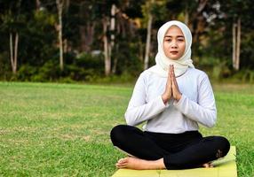jovem muçulmana asiática sentada na grama, praticando meditação foto