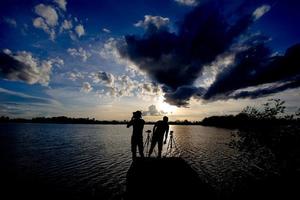 silhueta de dois homens no rio sob o pôr do sol foto