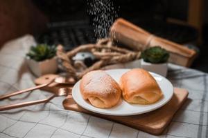 Pão de manteiga macio com açúcar de confeiteiro em um prato de madeira foto