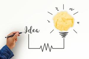 criatividade inspiração, ideias e conceitos de inovação com lâmpada e bola amassada de papel. mão do empresário escrevendo a ideia de texto com a caneta. foto