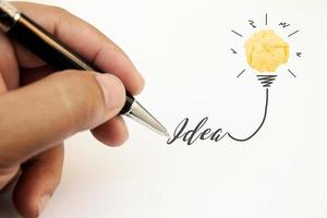 criatividade inspiração, ideias e conceitos de inovação com lâmpada e bola amassada de papel. mão do empresário escrevendo a ideia de texto com a caneta. foto