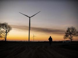 silhueta de um homem vai ao pôr do sol na direção das turbinas eólicas