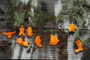 ramos de abeto, cortador de biscoitos de metal e figuras decorativas de Natal feitas de casca de laranja na velha mesa de madeira. foto