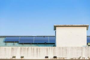 fotovoltaico solar painéis em construção cobertura em azul céu fundo, energia sistema eletricidade geração, alternativa energia conceito. foto