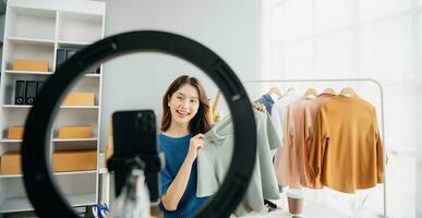 ásia senhora blogueiro mostrando roupas dentro frente do a Câmera para gravação vlog vídeo viver transmissão às dela fazer compras. foto