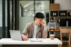 frustrado jovem empresário trabalhando em um laptop sentado em seu local de trabalho no escritório foto
