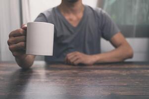 homem segurando um copo d'água, uma caneca de café, em uma mesa, em seu escritório foto