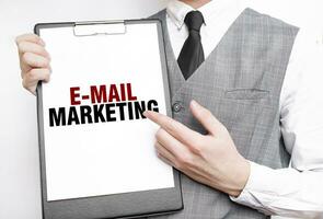 o email marketing inscrição em uma caderno dentro a mãos do uma homem de negocios em uma cinzento fundo, uma homem pontos com uma dedo para a texto foto