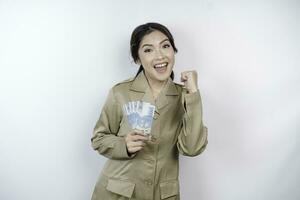 uma bem sucedido jovem governo trabalhador mulher é vestindo cáqui uniforme segurando dinheiro dinheiro dentro indonésio rupia isolado de branco fundo foto