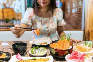jovem ásia mulher comendo sashimi conjunto dentro japonês restaurante foto