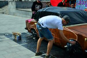 kharkov, ucrânia - 27 de maio de 2017 festival de arte de rua. jovens desenham grafite na carroceria do carro no centro da cidade. o processo de desenhar graffiti colorido em um carro com latas de aerossol foto