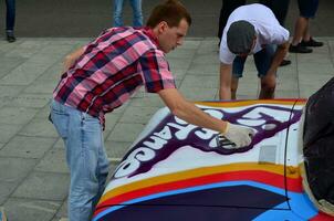 kharkov, ucrânia - 27 de maio de 2017 festival de arte de rua. jovens desenham grafite na carroceria do carro no centro da cidade. o processo de desenhar graffiti colorido em um carro com latas de aerossol foto