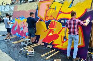 kharkov, ucrânia - 27 de maio de 2017 festival de artes de rua. jovens desenham grafite em paredes de madeira portáteis no centro da cidade. o processo de pintura em paredes com latas de aerossol foto