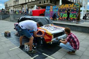 kharkov, ucrânia - 27 de maio de 2017 festival de arte de rua. jovens desenham grafite na carroceria do carro no centro da cidade. o processo de desenhar graffiti colorido em um carro com latas de aerossol foto