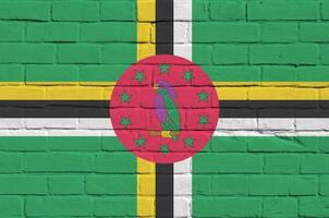 dominica bandeira retratado dentro pintura cores em velho tijolo muro. texturizado bandeira em grande tijolo parede alvenaria fundo foto