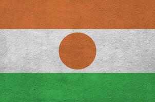 bandeira do niger retratada em cores brilhantes de tinta na parede de reboco em relevo antigo. banner texturizado em fundo áspero foto