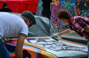 kharkov, ucrânia - 27 de maio de 2017 festival de arte de rua. jovens desenham grafite na carroceria do carro no centro da cidade. o processo de desenhar graffiti colorido em um carro com latas de aerossol foto